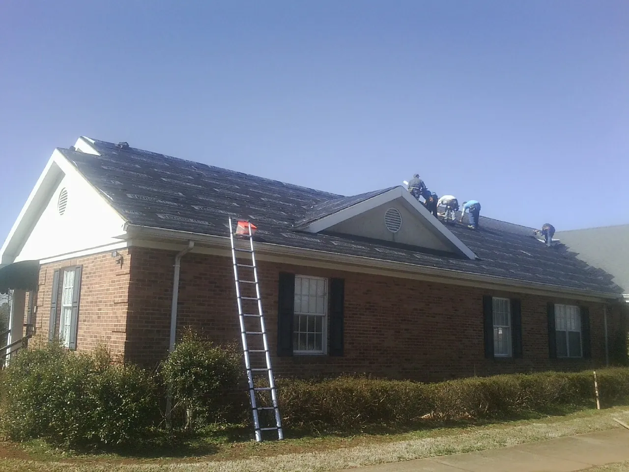 Crew tearing shingles off a brick ranch roof with a ladder set — Metal Roof Repair work by our crew in Valhalla