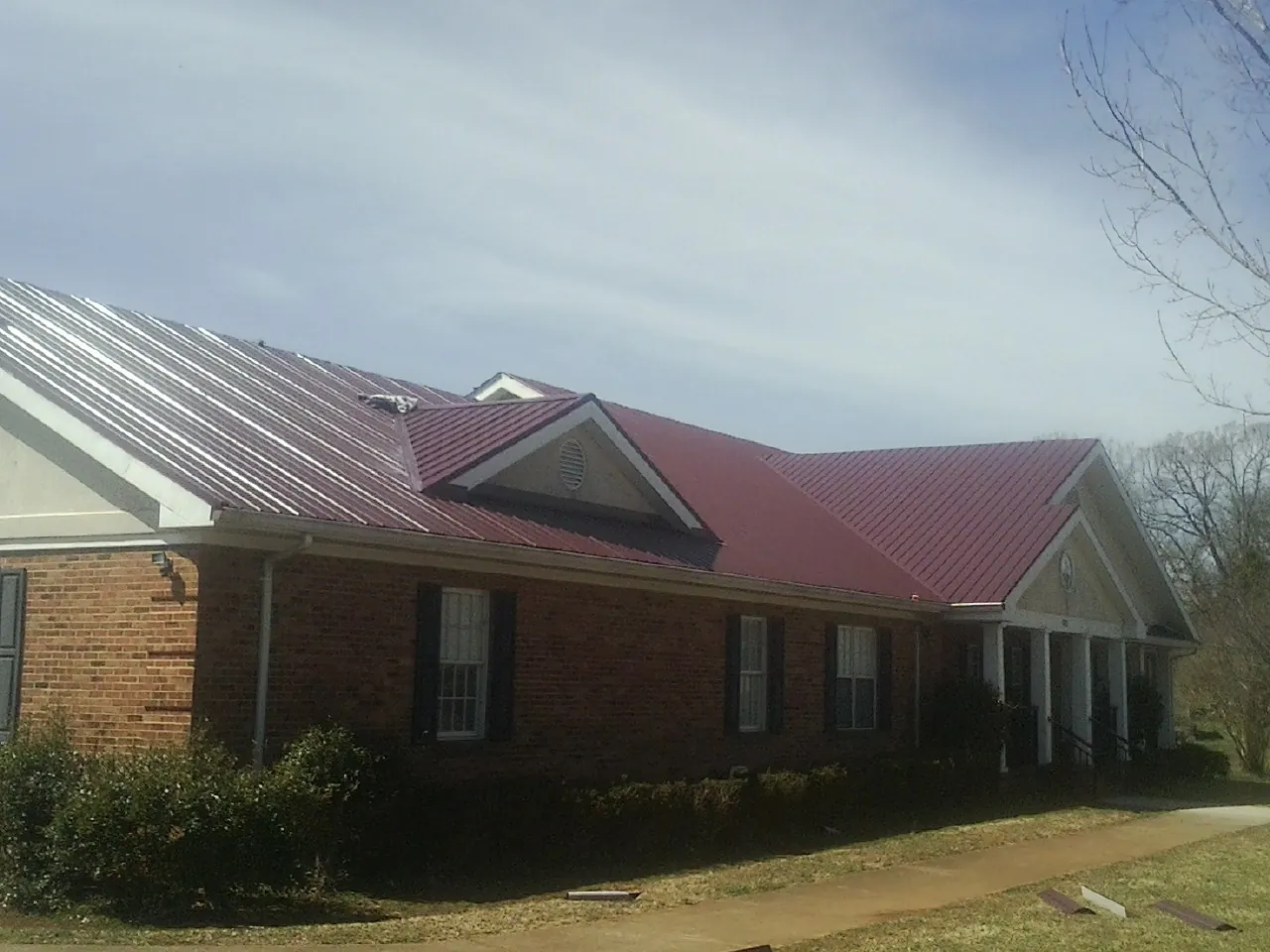Red metal roof with gabled entries on a long brick building, from a Hail Damage Roof Repair job in Valhalla