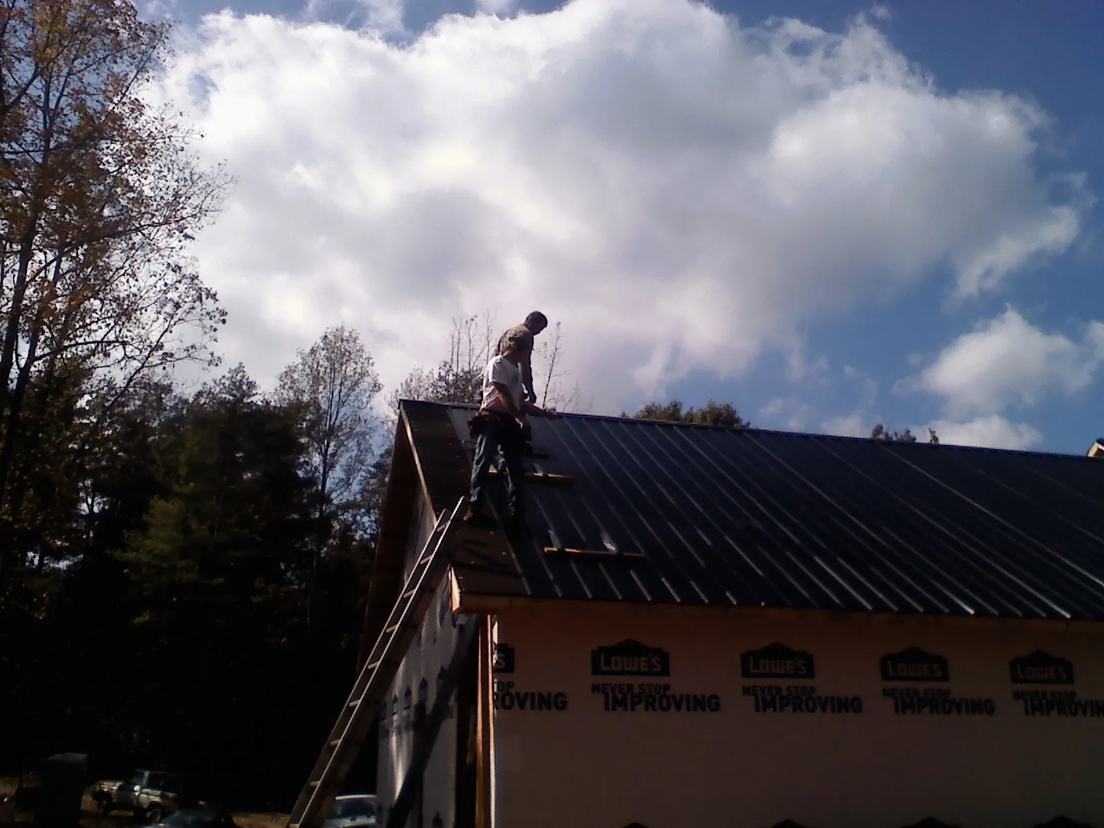 Roofer fastening dark metal panels high against a cloudy sky, from a Roof Inspection job in Valhalla