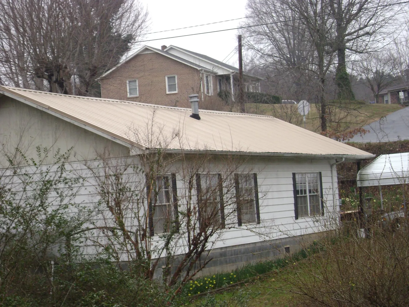 Tan metal roof on a white sided house set into a hillside — Commercial Roofing by Roofing Brothers in Valhalla